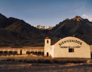 train stopped by a station building in front of Andean mountains at sunset