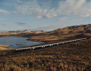 The train travels through russet grasslands overlooking the curves and contours of Lake Lagunillas, seen from a hill above.