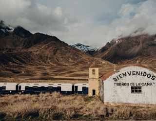 The Andean Explorer passes a highland rail stop with a white building painted with the words, Bienvenidos Señor de la Caña.