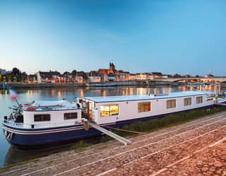 River barge moored on the opposite riverside of a lamplit French village at sunset