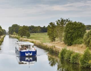 The white and blue Lilas barge cruises one of the peaceful waterways in France's Burgundy region, surrounded by nature.