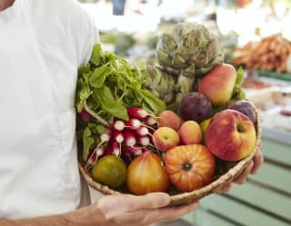 A chef holding a basket full of fresh vegetables 