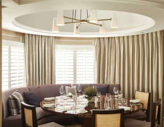 A circular turret nook is set for fine dining with crescent-shaped plump window seating and four chairs at a polished table