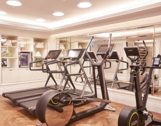 A mirror walled private gym with white towels on shelves and two treadmills, a Nordic cross trainer and stationary spin bike