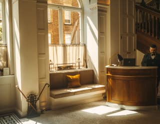 Sun pours through a window illuminating the lobby's timeless elegance with scallop mosaic floor and carved wood welcome desk.