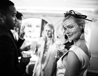 A woman in a light satin dress and dark net veil smiles at the camera in this black and white image of a vibrant party