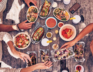 Birds-eye-view of hands reaching for dishes on a table laden with sharing platters and bar snacks