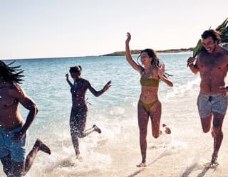 group of people running on the beach splashing water