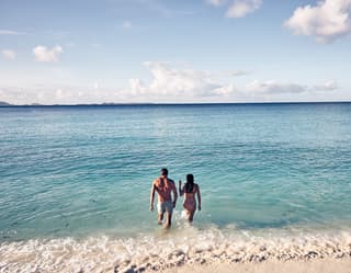 A couple strolling from the shore into the calm turquoise sea before them