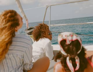 Soft-focus, eye-level view of three women lying on the sundeck of a yacht looking through the taffrail out at the sea.