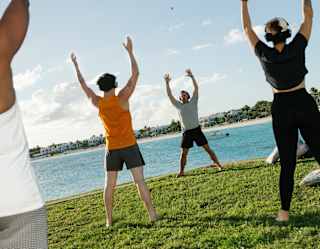 Angled image of three guests standing, arms raised as they follow the guidance of a yoga instructor, during a seafront class.