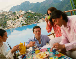Angled shot of a group of guests in soft-focus as they enjoy food at the infinity pool bar with a Lattari mountains backdrop.