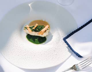 Close-up of white fish served with asparagus and seaweed jus on a circular white dish