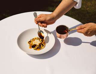 A chef spoons sauce from a copper pan over five exquisite tortellini, served on a textured plate at Belvedere, seen close-up.