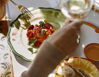 Seen from above, a guest raises a glass of white wine above a vibrant plate of spaghetti Ravello with tomatoes and basil.