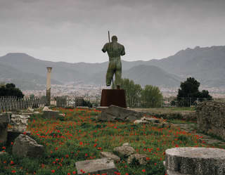 Giant bronze statue of a warrior among a field of poppies and scattered rocks in Pompeii