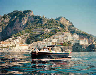 A group of friends enjoys a coastline tour aboard a beautiful black wooden boat as it cruises by pretty cliff-side towns.