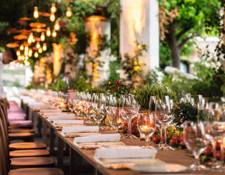 Rows of shimmering wine glasses on a long candlelit banquet table under a gazebo