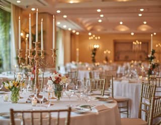 Circular banquet tables lit with candelabras and set for a wedding in an elegant room