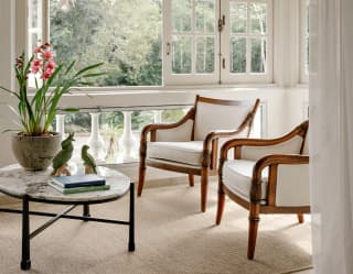 View over a terrace-cum-sunroom with two lounge chairs, a low table with pot-plant, balustrade rail and open bifold windows.