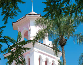 The immaculately restored Hotel das Cataratas colonial-style bell tower between mature palm trees and cloudless blue sky