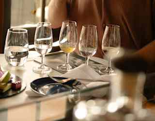 Close-up of five glasses, four with clear liquid and another with a pale yellow drink, seen during a Cachaca tasting session.