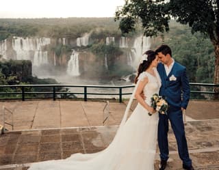 Young bride and groom affectionately embrace on the paved terrace in front of Iguassu Falls