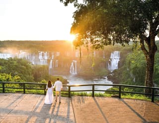 a couple in the distance standing in front of iguassu falls
