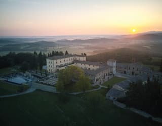 The sun creeps above mist shrouded hills to reveal the ancient pale yellow and stone walls of the Castello di Casole hotel