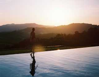 A guest's silhouette merges with the darkening hills as they walk the pool's edge, reflection caught in the still water.