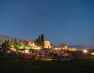 Guests stand around a telescope in the ancient stone amphitheatre for a stargazing experience, with the hotel lit up behind.