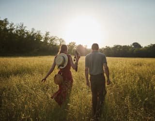 Lady in a red dress walking through a grassy field with a guide at sunrise