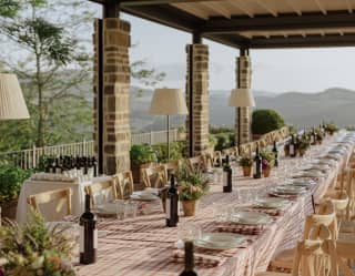 Long banquet table set for lunch under a shaded pergola with countryside views