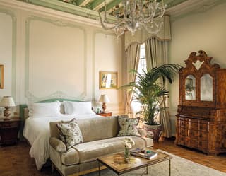 An 18th Century walnut armoire hugs the wall. At the foot of the king bed, a silvery velvet sofa with Chinoiserie cushions