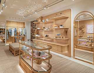 View of the Dior boutique, with rattan wall panels, rails and floating shelves around a central three-tier glass table.