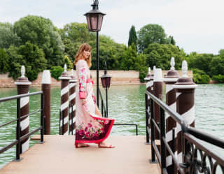 A woman in a floral silk kimono looks back from a jetty flanked by white and brown candy-striped paline de casada