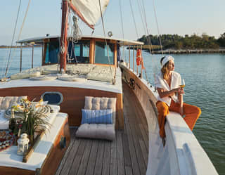 Lady perched on the edge of a luxurious sailing yacht at sunset