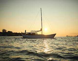The setting sun sends a path of gold across the lagoon. A yacht with dropped anchor and lowered sail enjoys the view