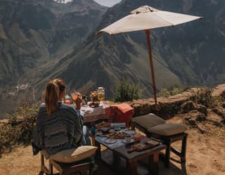 A female guest enjoys breakfast under a sunshade at makeshift tables on the rim of Peru’s Colca Canyon