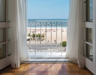 Billowing white voile curtains frame the oatmeal, cobalt, azure horizontal stripes that are the beach, sea and sky view
