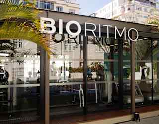Front view of the BioRitmo gym with large signage and windowed front, offering glimpses of treadmills and reflecting the sunlight.