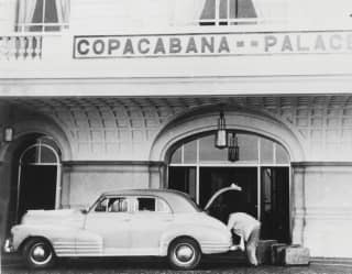 In a vintage image from the 1950s, a doorman unloads leather valises from a classic Chevrolet outside the hotel's entrance