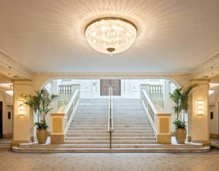 A marble staircase, flanked by palms and lit by a bowl chandelier descends into the lobby of the Copacabana Palace Theatre