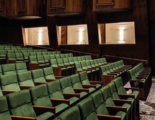 Neat rows of green velvet fold-down theatre chairs climb the gentle incline of the floor, watched by wood panelled boxes