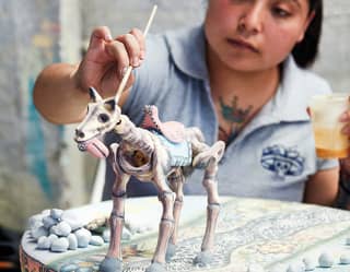 Artist in a studio putting the finishing touches on a ceramic 'day of the dead' style horse figurine