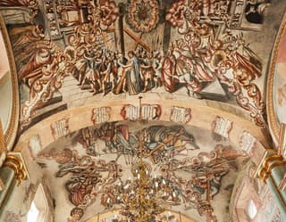 Vaulted ceiling of a temple covered in ornate Mexican Baroque murals of Jesus carrying the cross