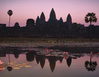 Cambodia's iconic temple, Angkor Wat, is silhouetted against a lilac sundown sky and reflected in the lily-filled moat below.
