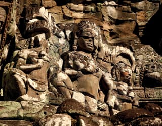 An ancient stone wall carving detail with three figures, from the culturally-rich Siem Reap province of Cambodia.