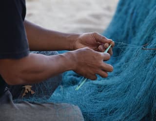 The skilled hands of a fisherman mending his blue nets in the village of Jimbaran in Bali, famous for its fish markets.