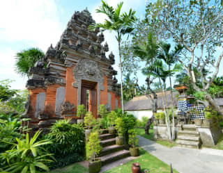 A Kori Agung ornate stone entrance gate with orange walls and a narrow doorway with a Balinese god carving above the lintel.